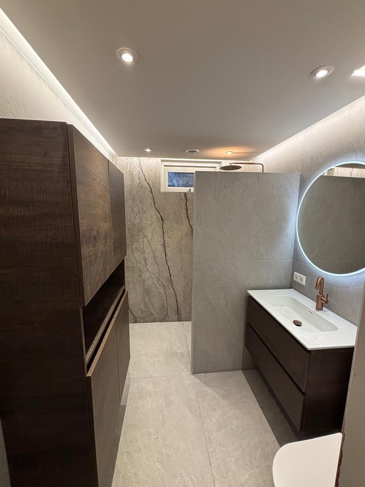 Prefab badkamer met natuursteen wand, donkere meubels en koperen kranen